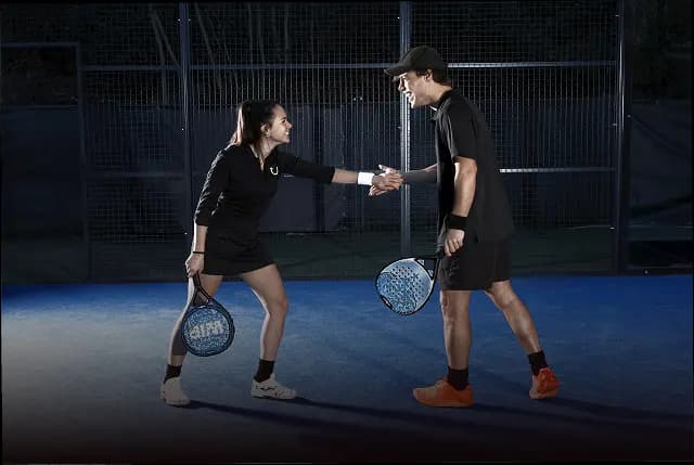 Dua pemain padel bersalaman di tengah lapangan indoor setelah pertandingan