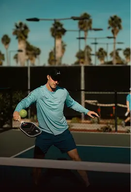 Pemain padel memukul forehand di lapangan outdoor pada siang hari